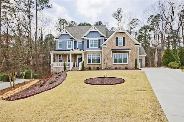 craftsman inspired home featuring concrete driveway, covered porch, a front yard, board and batten siding, and brick siding