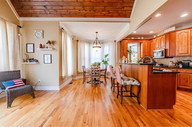 kitchen featuring hanging light fixtures, light wood-type flooring, tasteful backsplash, a kitchen bar, and kitchen peninsula