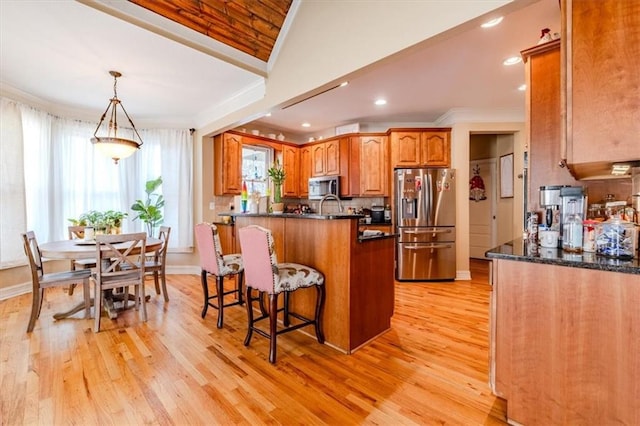 kitchen featuring ornamental molding, hanging light fixtures, light wood-type flooring, and appliances with stainless steel finishes