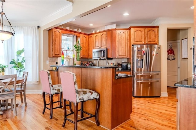 kitchen featuring pendant lighting, light hardwood / wood-style floors, crown molding, and stainless steel appliances