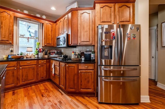 kitchen featuring dark stone countertops, decorative backsplash, light hardwood / wood-style floors, and appliances with stainless steel finishes