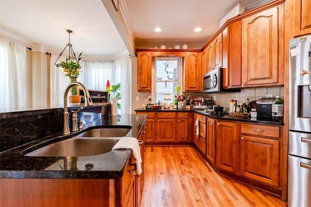 kitchen featuring sink, ornamental molding, appliances with stainless steel finishes, decorative light fixtures, and light hardwood / wood-style floors