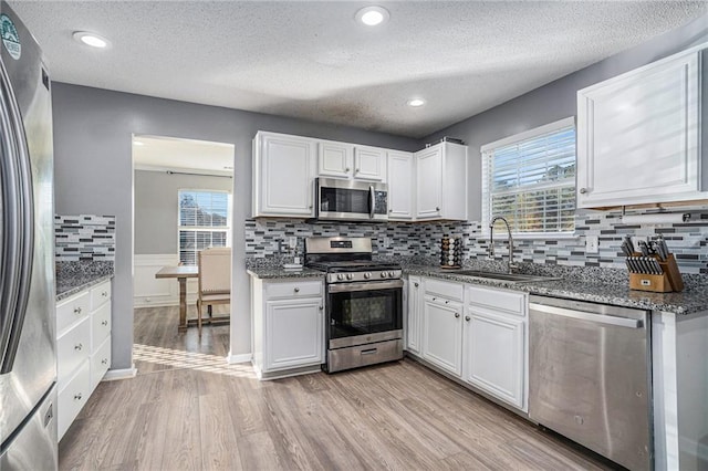 kitchen with white cabinets, a healthy amount of sunlight, appliances with stainless steel finishes, and light hardwood / wood-style flooring