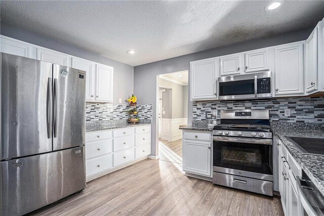 kitchen with dark stone counters, white cabinets, decorative backsplash, light wood-type flooring, and appliances with stainless steel finishes