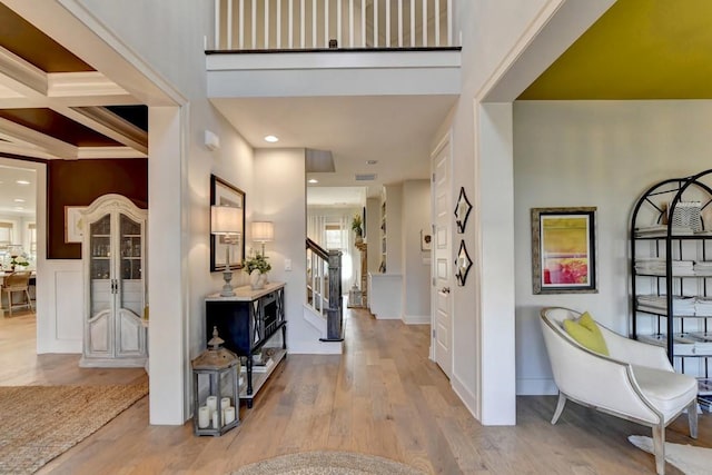 entrance foyer with beam ceiling, light hardwood / wood-style flooring, coffered ceiling, and crown molding