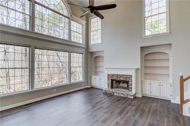 unfurnished living room with a stone fireplace, a wealth of natural light, visible vents, and ceiling fan