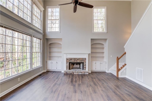 unfurnished living room featuring a stone fireplace, stairs, ceiling fan, and baseboards