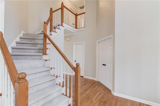 stairs featuring baseboards, visible vents, wood finished floors, and a towering ceiling