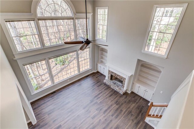 living area with dark wood-style flooring, visible vents, a fireplace, a ceiling fan, and a high ceiling