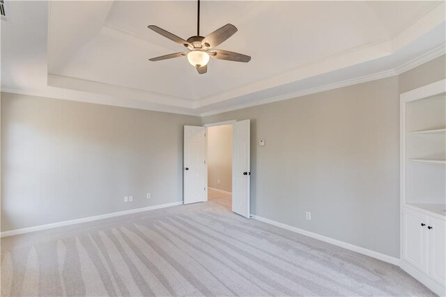 unfurnished room with baseboards, ornamental molding, a ceiling fan, a raised ceiling, and light colored carpet