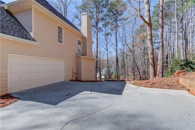 view of home's exterior featuring driveway, an attached garage, and a chimney