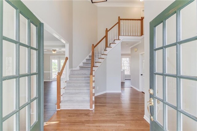 foyer with stairway, a high ceiling, wood finished floors, ceiling fan, and ornamental molding