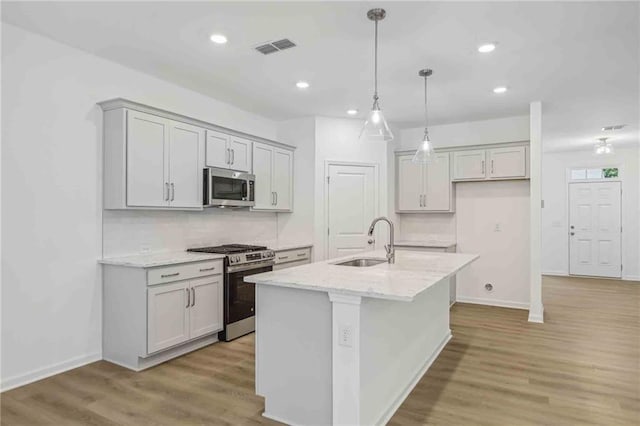 kitchen with sink, light hardwood / wood-style flooring, an island with sink, appliances with stainless steel finishes, and light stone counters