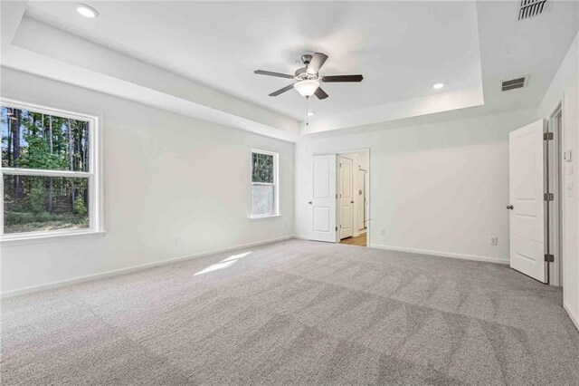 unfurnished bedroom with light carpet, a tray ceiling, multiple windows, and ceiling fan