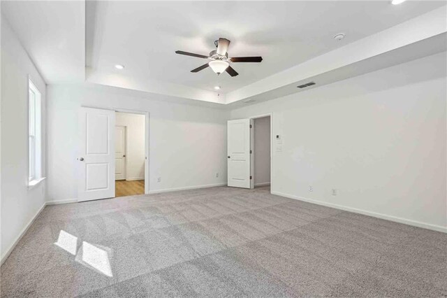 unfurnished bedroom featuring a tray ceiling, ceiling fan, and light colored carpet