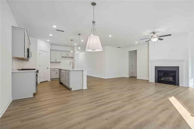 kitchen with a center island with sink, decorative light fixtures, light wood-type flooring, and sink