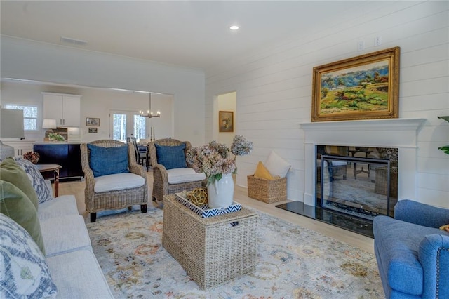 living room featuring a chandelier, a glass covered fireplace, ornamental molding, light wood-style flooring, and recessed lighting