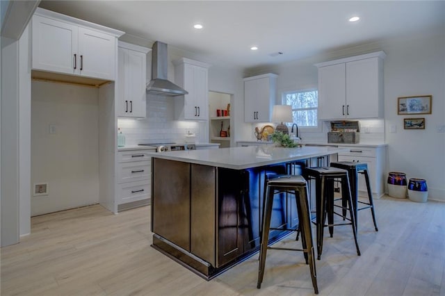 kitchen featuring wall chimney range hood, backsplash, a center island, white cabinets, and light countertops