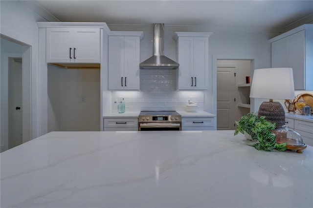 kitchen featuring wall chimney exhaust hood, stainless steel electric range, light stone counters, decorative backsplash, and white cabinets