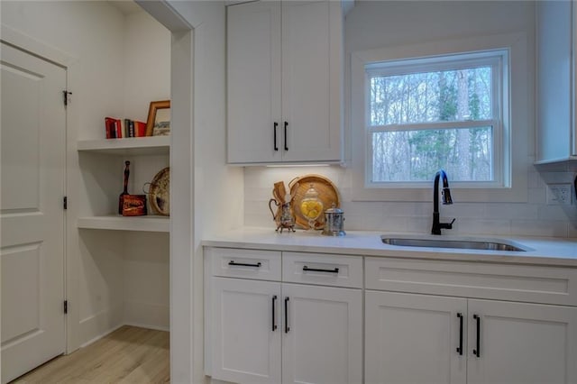 kitchen with a sink, decorative backsplash, light countertops, and white cabinetry