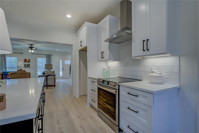 kitchen featuring wall chimney exhaust hood, stainless steel electric range, light countertops, tasteful backsplash, and light wood-type flooring