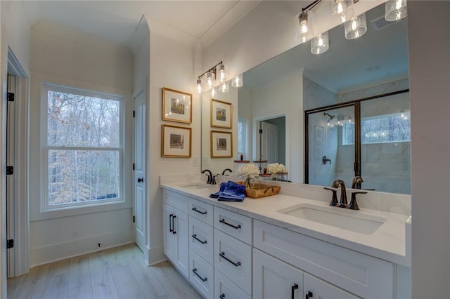 bathroom with a shower stall, wood finished floors, double vanity, and ornamental molding