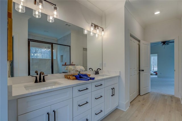 full bathroom featuring a stall shower, wood finished floors, crown molding, a ceiling fan, and double vanity