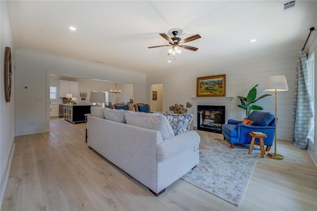 living room with light wood-style flooring, a ceiling fan, a glass covered fireplace, a chandelier, and recessed lighting