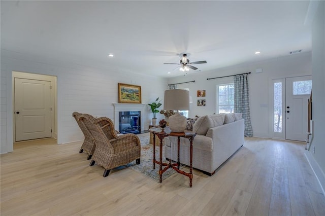 living area with light wood-style floors, a glass covered fireplace, ceiling fan, recessed lighting, and baseboards