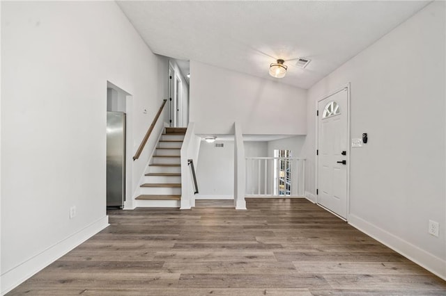 foyer with stairs, wood finished floors, visible vents, and baseboards