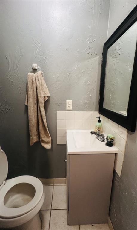 half bath with tile patterned flooring, a textured wall, vanity, and toilet