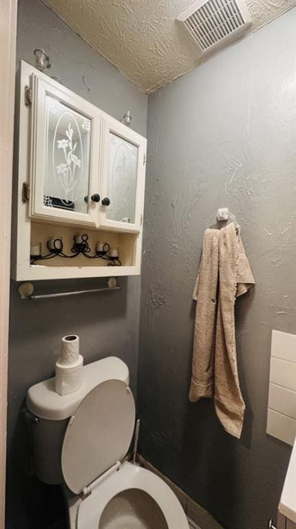 bathroom featuring visible vents, a textured wall, a textured ceiling, and toilet