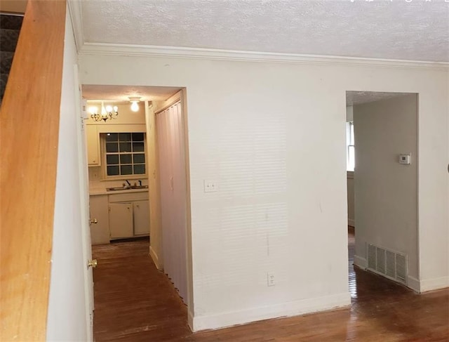 hallway featuring a textured ceiling, wood finished floors, a sink, visible vents, and ornamental molding