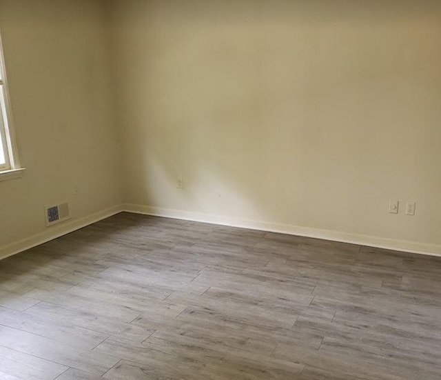 empty room featuring wood finished floors, visible vents, and baseboards