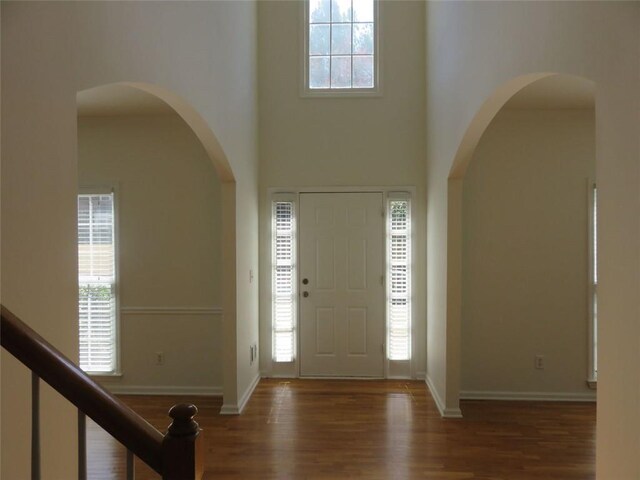 foyer with baseboards, a high ceiling, wood finished floors, and arched walkways