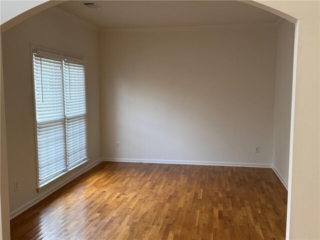 spare room featuring crown molding, wood finished floors, arched walkways, and baseboards