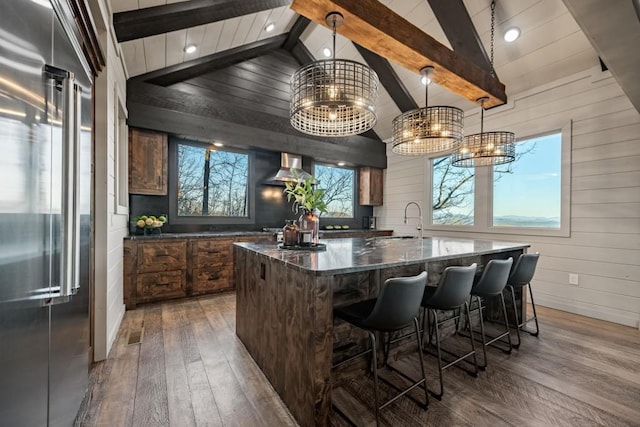 bar featuring wall chimney exhaust hood, high end refrigerator, lofted ceiling with beams, dark stone countertops, and pendant lighting