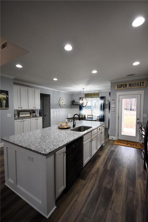 kitchen featuring visible vents, a center island with sink, black dishwasher, white cabinetry, and a sink