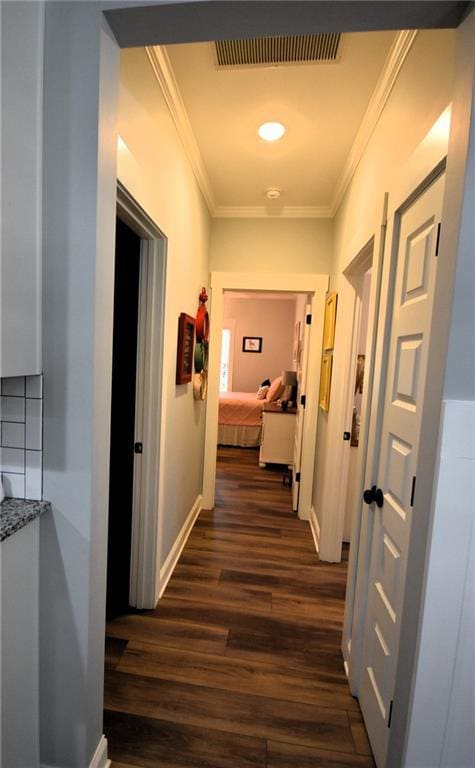 hall with visible vents, baseboards, dark wood-type flooring, and ornamental molding