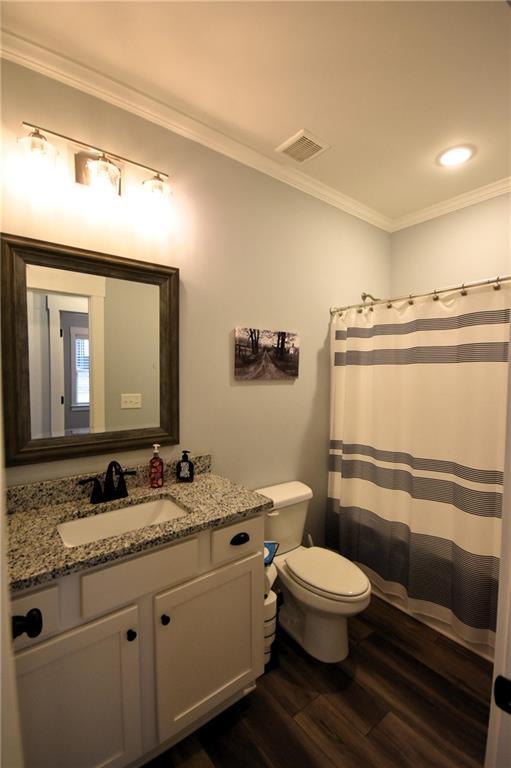 bathroom with visible vents, toilet, wood finished floors, and ornamental molding