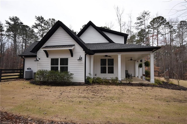 view of front facade with a front lawn, a ceiling fan, fence, board and batten siding, and a shingled roof