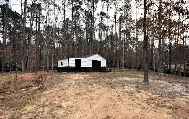 view of yard with an outdoor structure, fence, a forest view, and an outbuilding