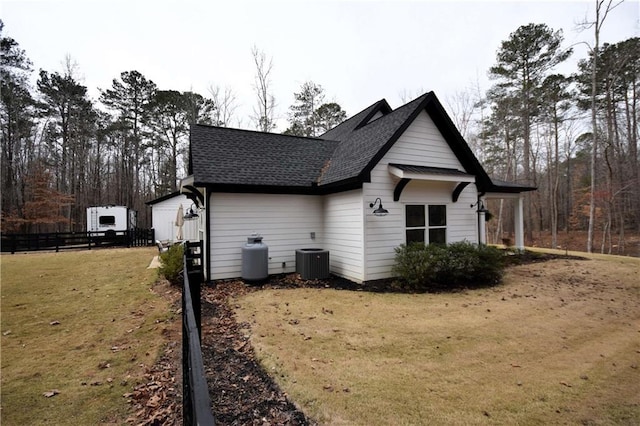 view of side of home featuring a yard, central AC unit, roof with shingles, and fence