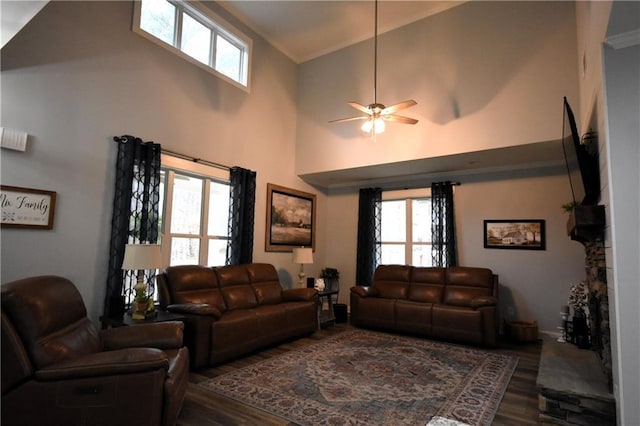 living room featuring a ceiling fan, wood finished floors, a towering ceiling, and a healthy amount of sunlight