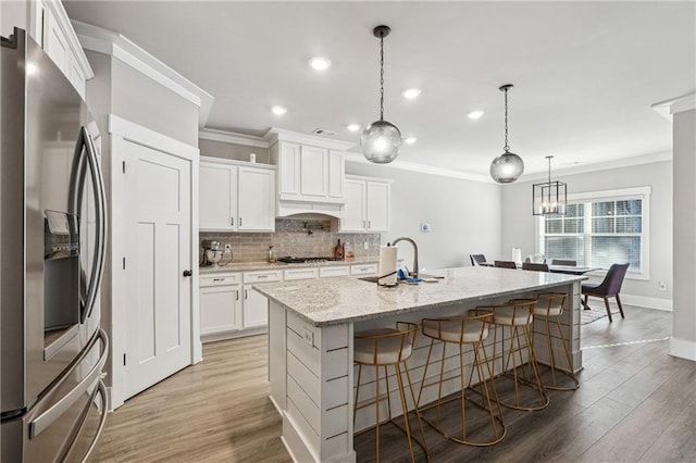 kitchen featuring white cabinets, a breakfast bar area, hanging light fixtures, a center island with sink, and appliances with stainless steel finishes