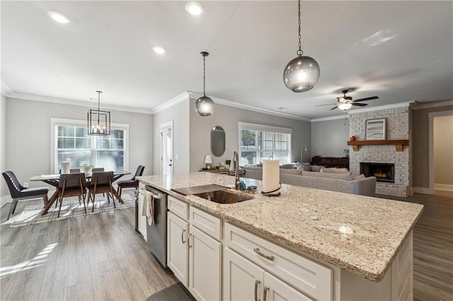 kitchen featuring hanging light fixtures, an island with sink, a brick fireplace, sink, and stainless steel dishwasher