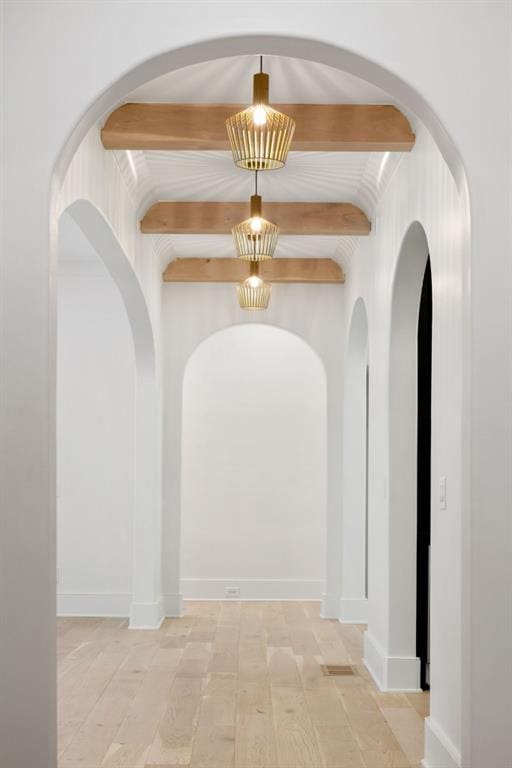 hall featuring light wood-type flooring, beam ceiling, and a notable chandelier