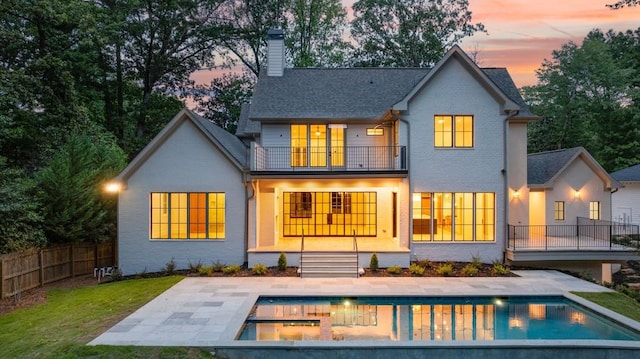 back house at dusk featuring a fenced in pool, a patio area, and a balcony