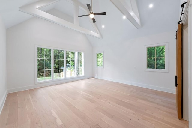 interior space with a barn door, ceiling fan, light hardwood / wood-style flooring, and high vaulted ceiling