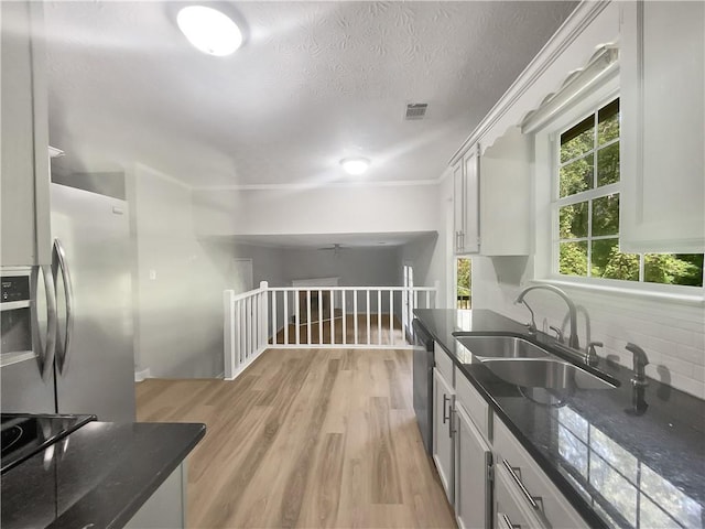 kitchen with tasteful backsplash, white cabinetry, light wood-type flooring, stainless steel appliances, and sink